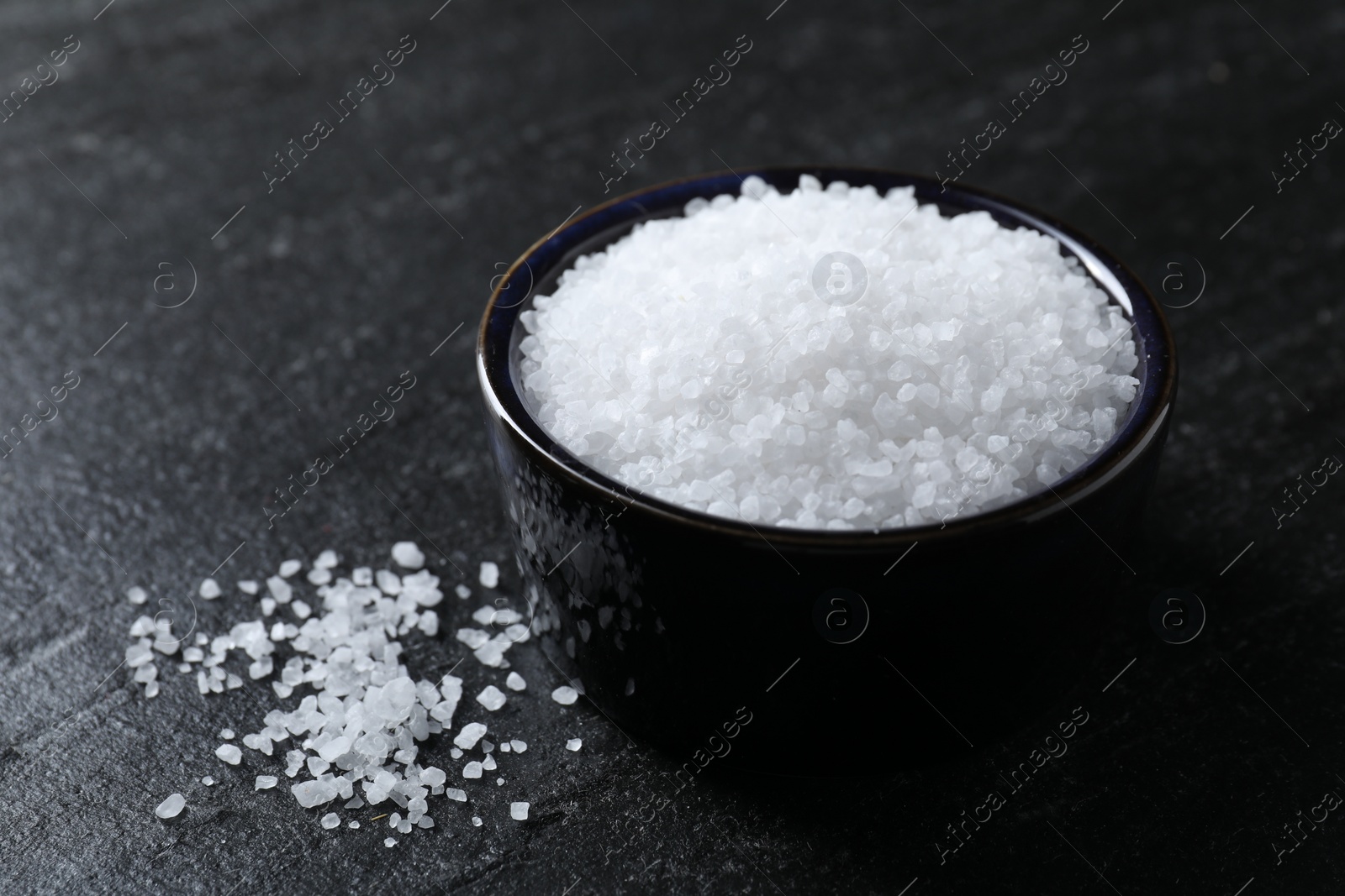 Photo of Organic white salt in bowl on black table