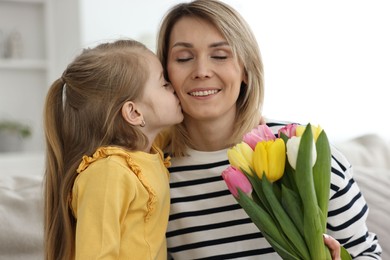 Photo of Little daughter kissing and congratulating her mom with Mother`s Day at home. Woman holding bouquet of beautiful tulips