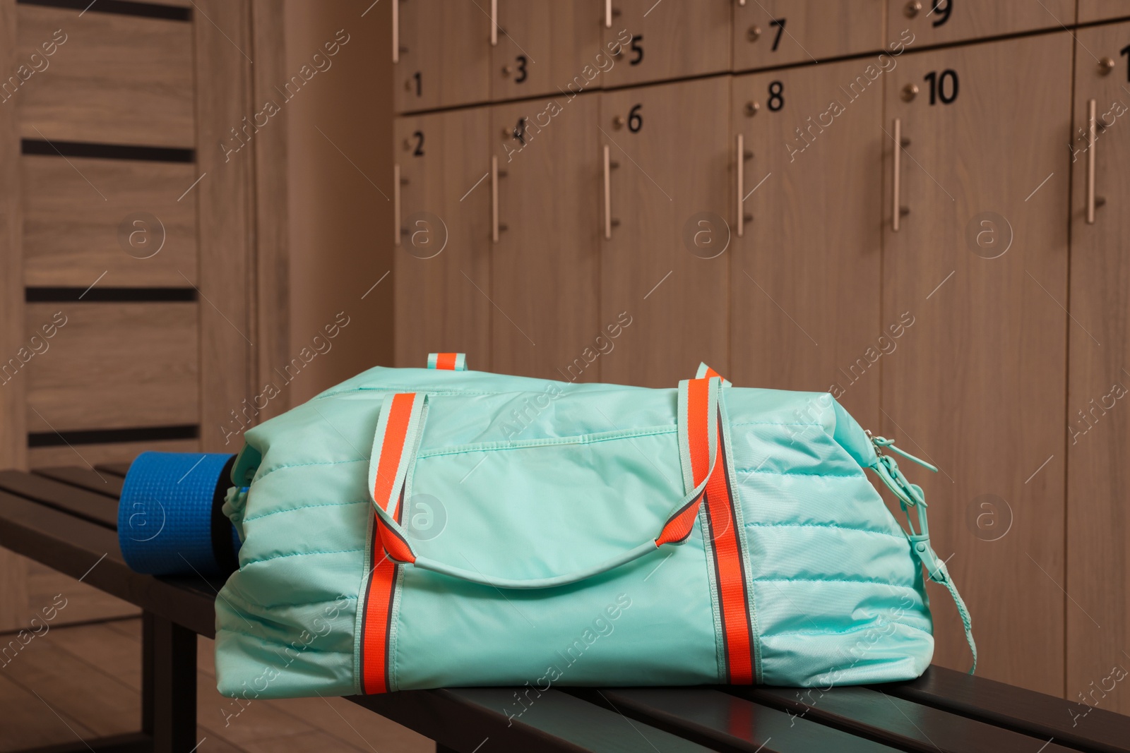 Photo of Sports bag and yoga mat on wooden bench in locker room