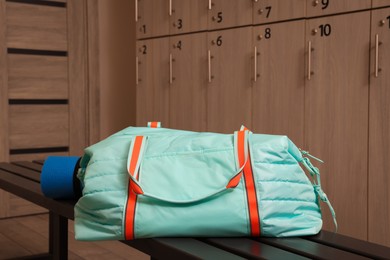 Photo of Sports bag and yoga mat on wooden bench in locker room