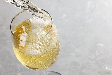 Photo of Pouring tasty aromatic wine in glass at gray marble table, closeup. Space for text