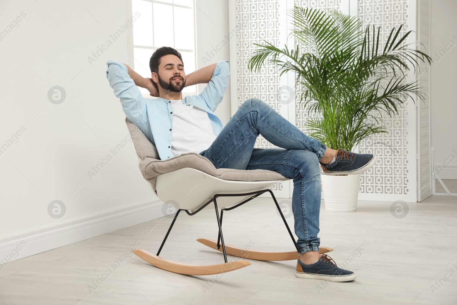 Photo of Young man relaxing in rocking chair at home