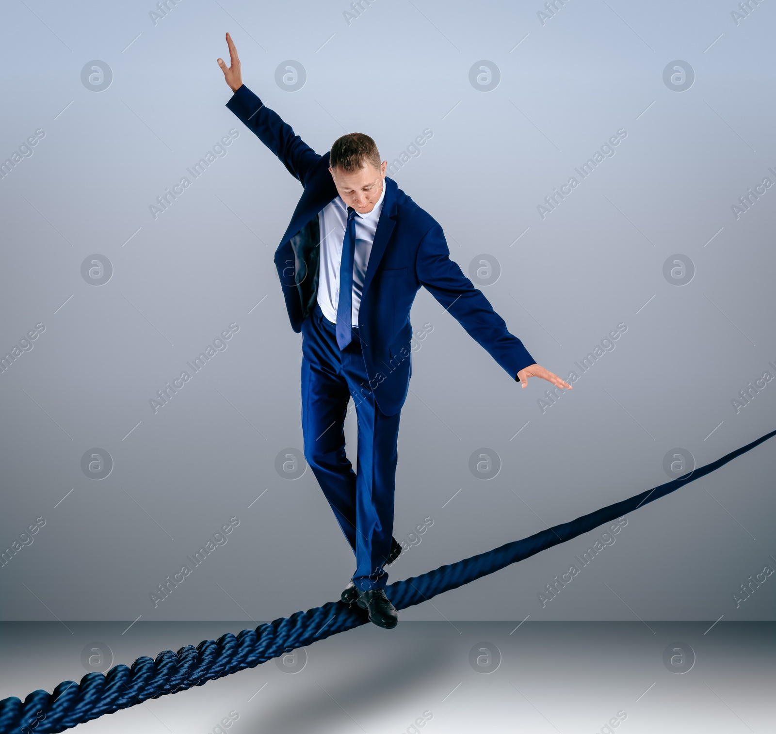 Image of Risks and challenges of entrepreneurship. Businessman balancing on rope against grey background