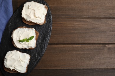 Photo of Bread with cream cheese on wooden table, top view. Space for text