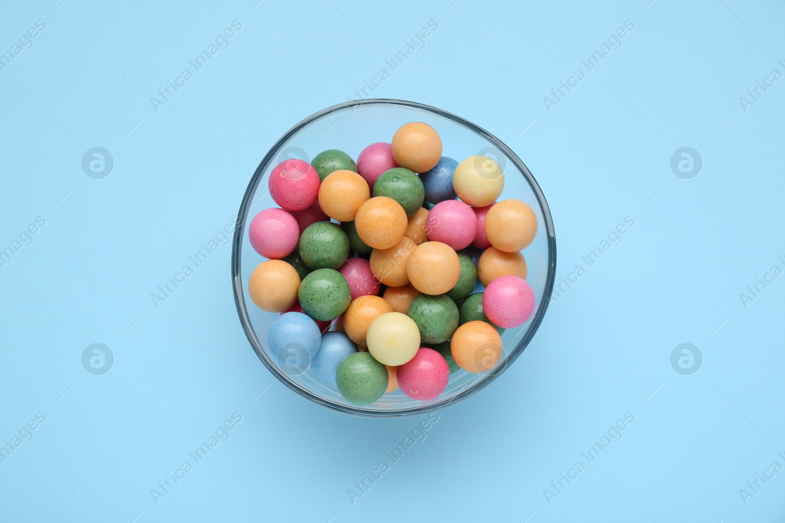 Photo of Bowl with many bright gumballs on light blue background, top view