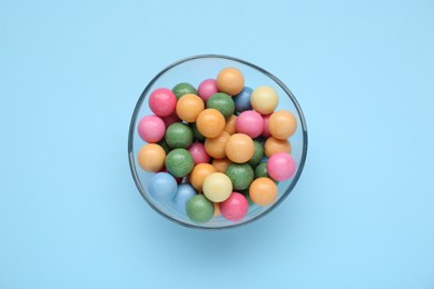 Bowl with many bright gumballs on light blue background, top view