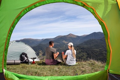 Photo of Couple with drinks enjoying mountain landscape, view from camping tent