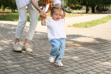 Photo of Mother supporting daughter while she learning to walk outdoors, closeup. Space for text