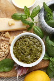 Photo of Tasty pesto sauce in bowl, basil, pine nuts, garlic and cheese on table, top view