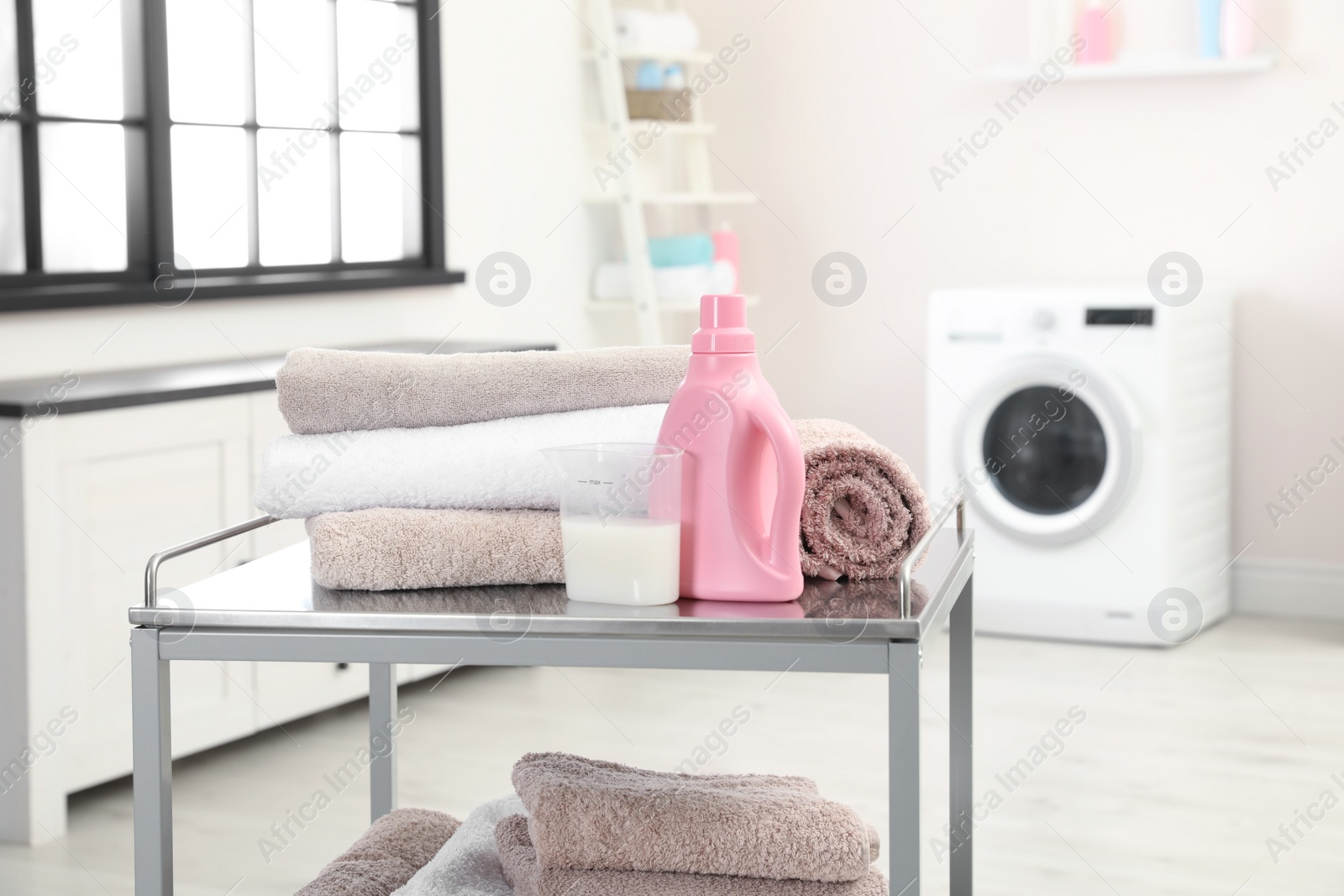 Photo of Soft bath towels and detergent on metal cart against blurred background