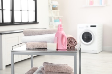 Soft bath towels and detergent on metal cart against blurred background