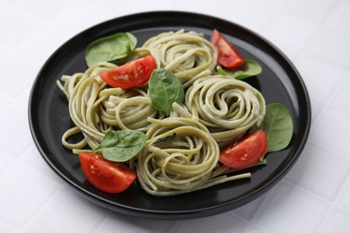 Photo of Tasty pasta with spinach, sauce and tomatoes on white tiled table, closeup