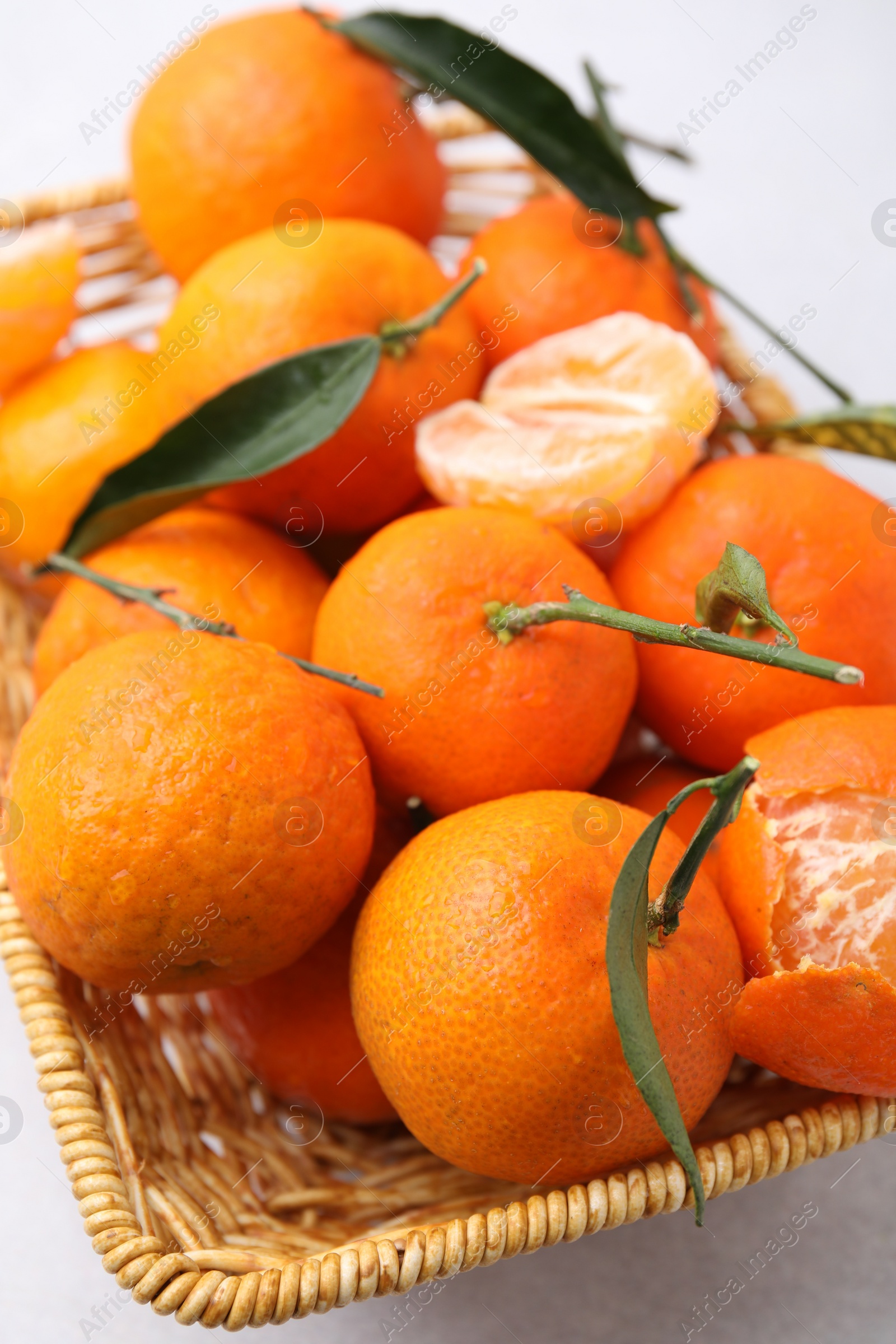 Photo of Fresh ripe tangerines with green leaves in wicker basket on white table, closeup