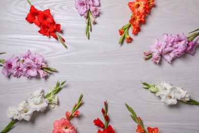 Photo of Flat lay composition with beautiful gladiolus flowers on wooden background. Space for text