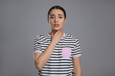 Photo of Young woman suffering from sore throat on grey background. Cold symptoms