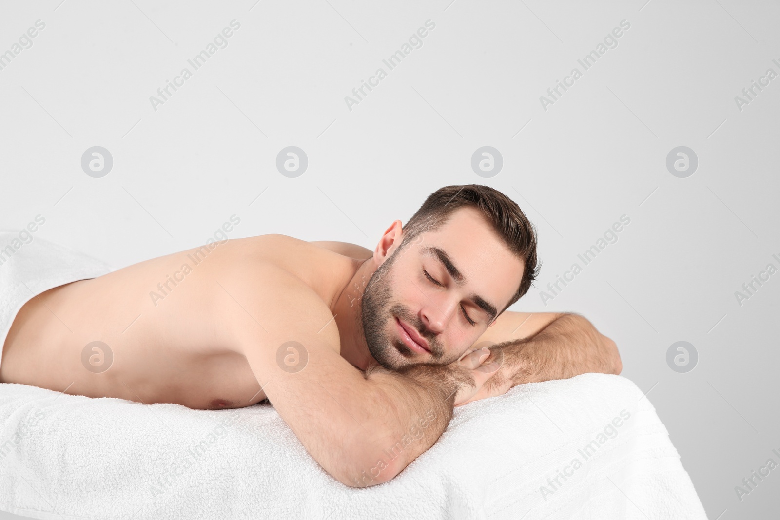 Photo of Handsome man relaxing on massage table against white background. Spa service