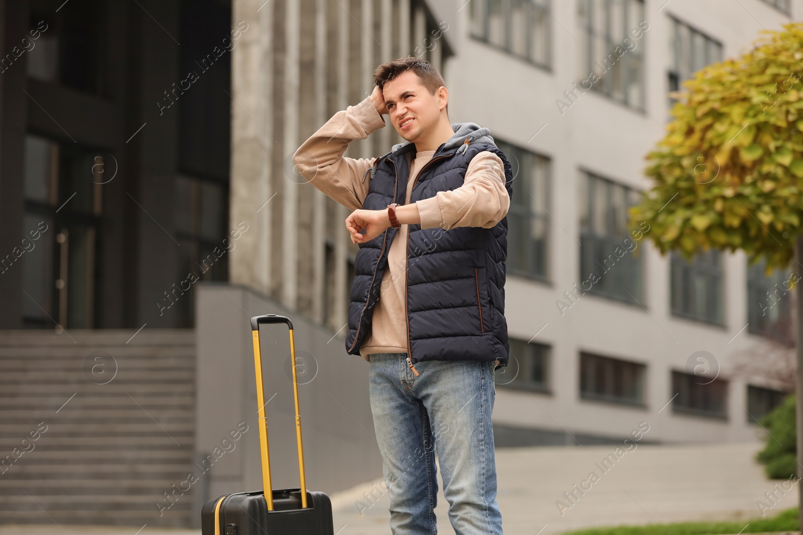 Photo of Being late. Worried man with suitcase near building outdoors