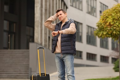 Being late. Worried man with suitcase near building outdoors