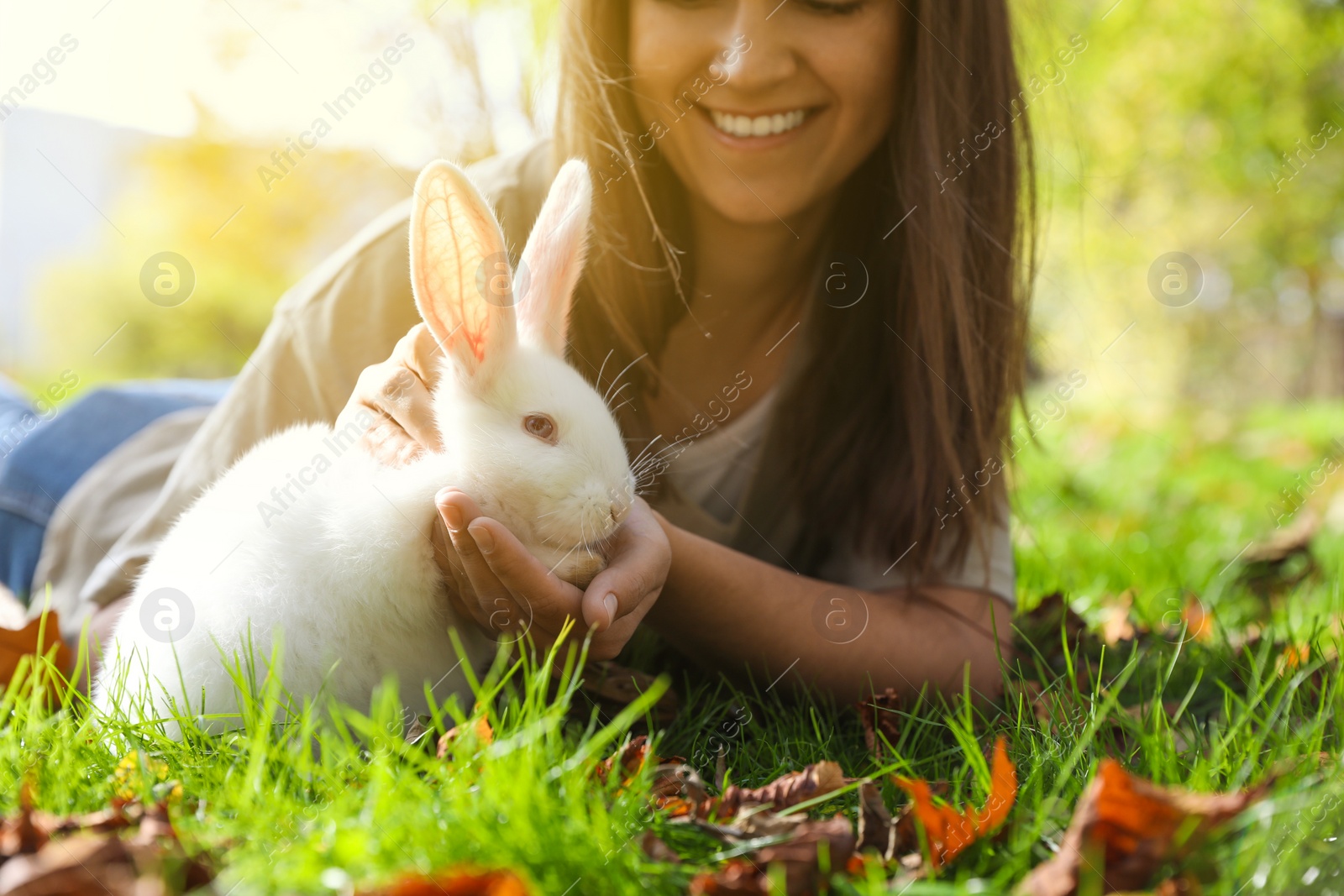 Photo of Happy woman with cute white rabbit on grass in park, closeup