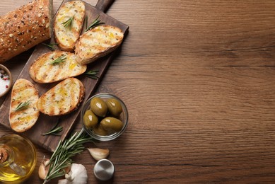 Tasty bruschettas with oil and rosemary on wooden table, flat lay. Space for text