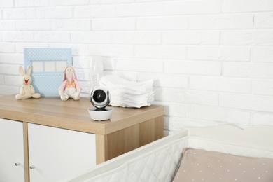 Photo of Baby camera and accessories on chest of drawers near crib in room, space for text. Video nanny