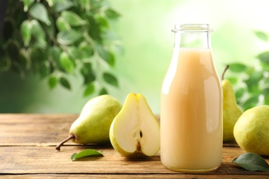 Photo of Fresh pear juice in glass bottle and fruits on wooden table, closeup. Space for text