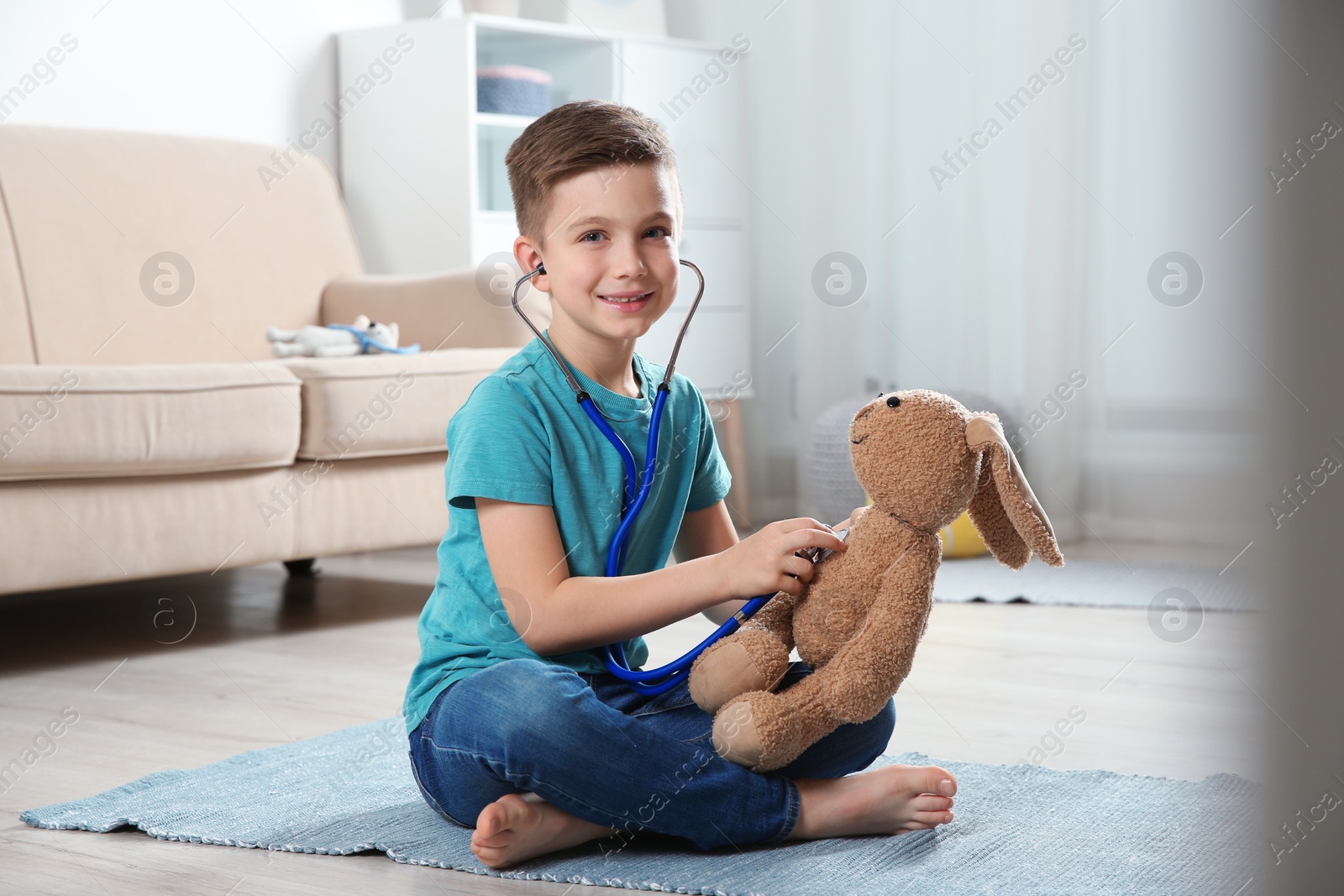 Photo of Cute child imagining himself as doctor while playing with stethoscope and toy bunny at home