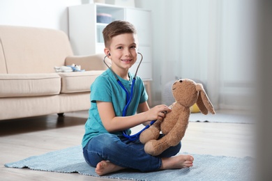 Cute child imagining himself as doctor while playing with stethoscope and toy bunny at home