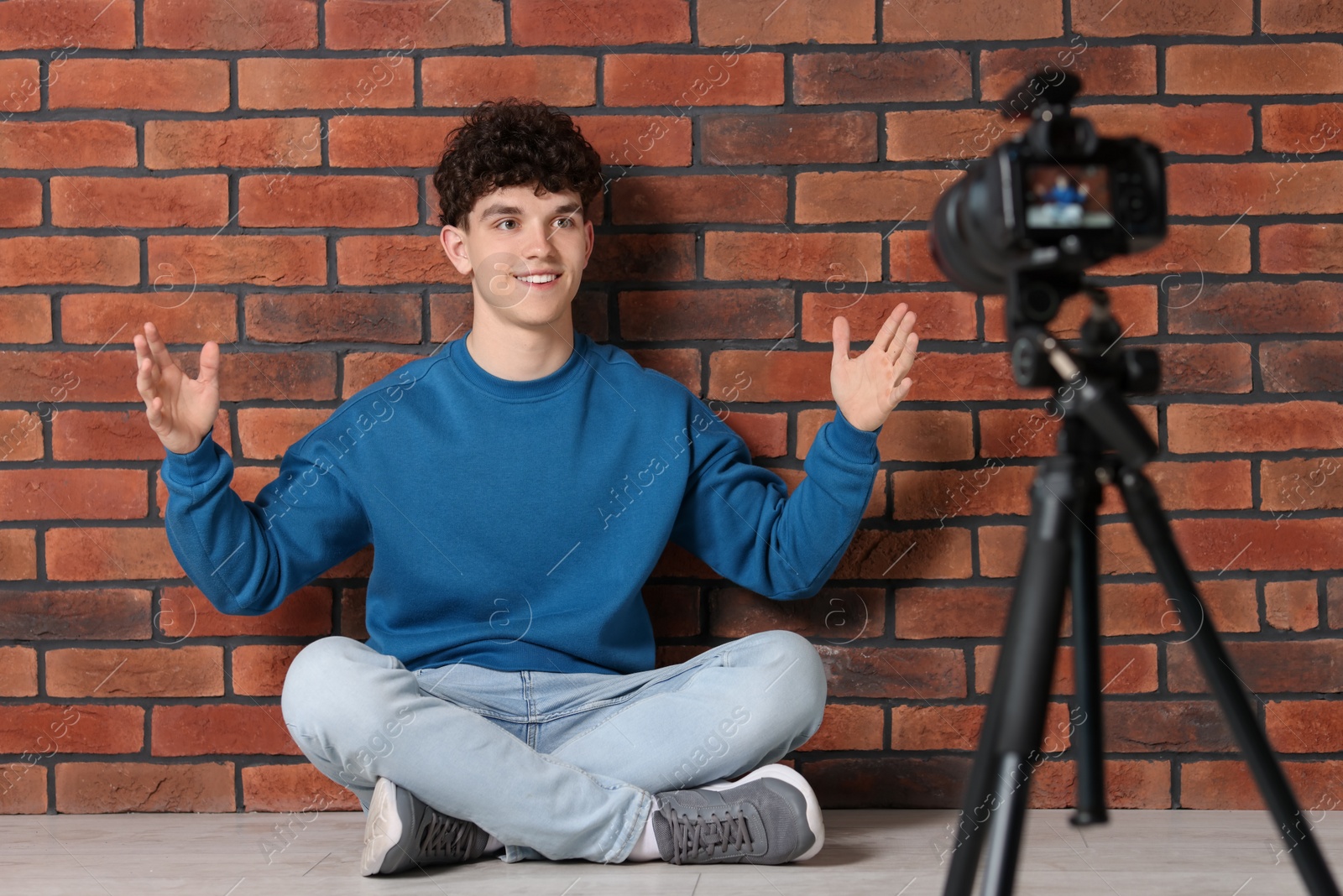 Photo of Smiling teenage blogger explaining something while streaming indoors