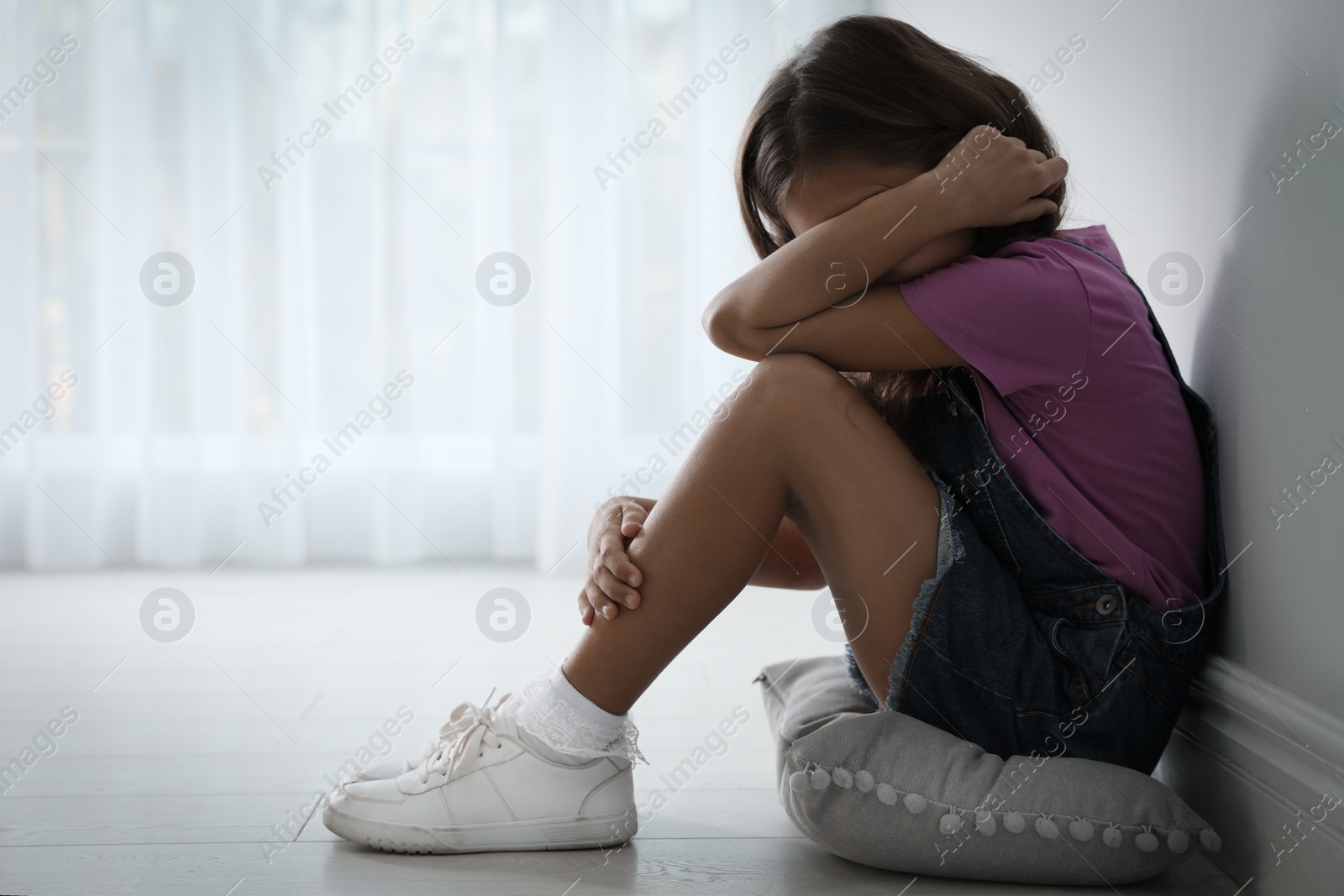 Photo of Scared little girl near white wall indoors, space for text. Domestic violence concept