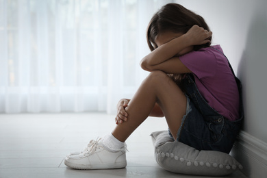 Photo of Scared little girl near white wall indoors, space for text. Domestic violence concept