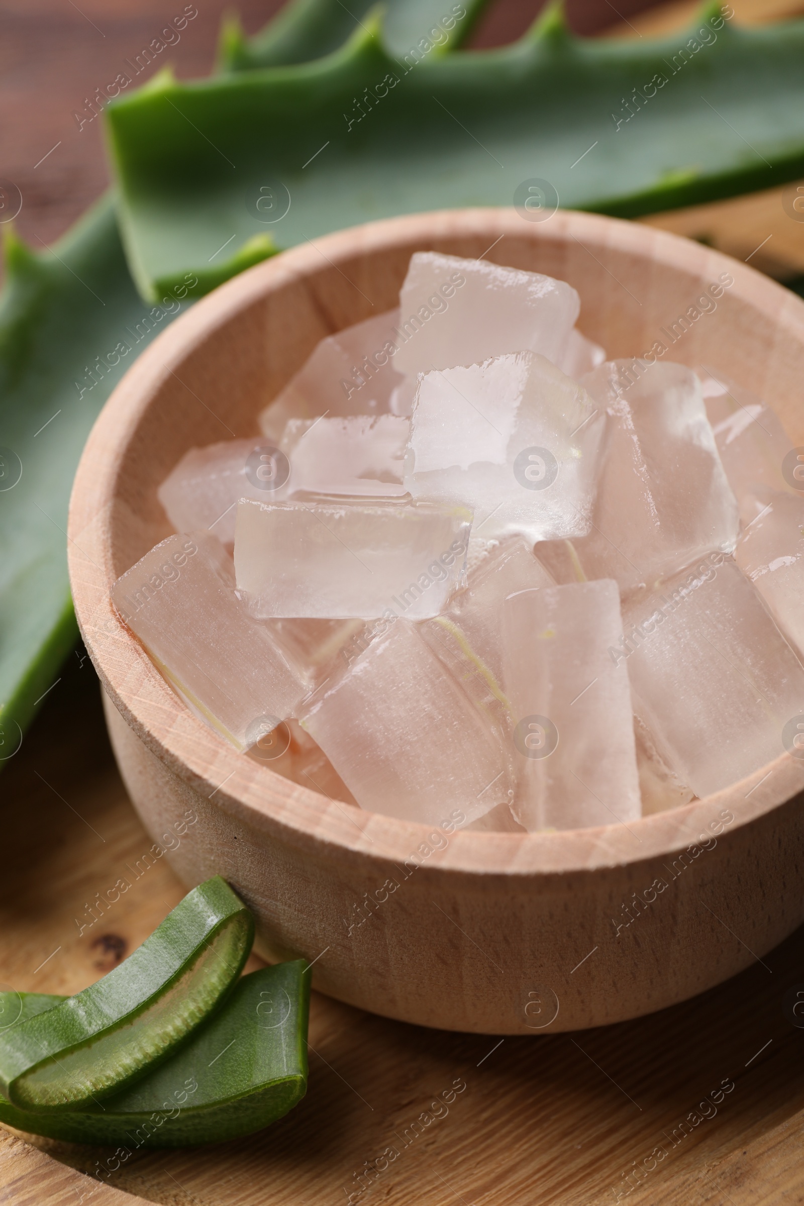 Photo of Aloe vera gel and slices of plant on wooden table, closeup