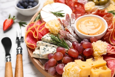 Photo of Wooden plate with different delicious snacks on white marble table, closeup