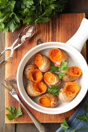 Delicious cooked snails served on wooden table, flat lay