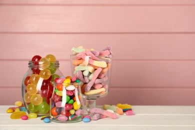 Photo of Jars with different delicious candies on white wooden table against pink background, space for text