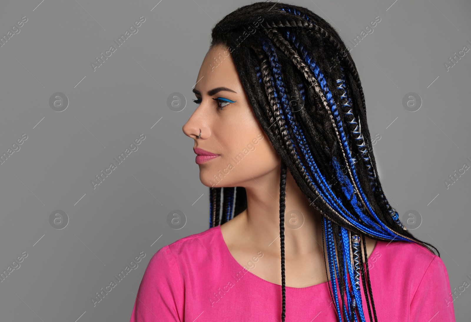 Photo of Beautiful young woman with nose piercing and dreadlocks on grey background