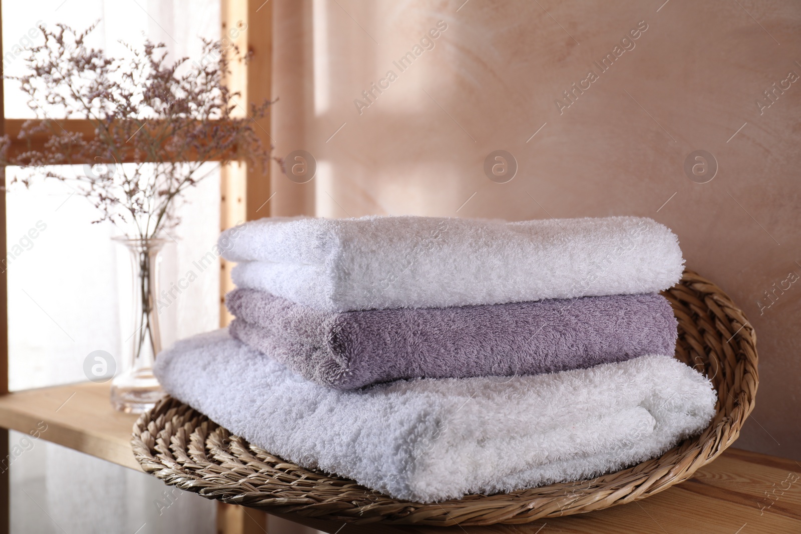 Photo of Stacked soft towels and flowers on wooden shelf indoors