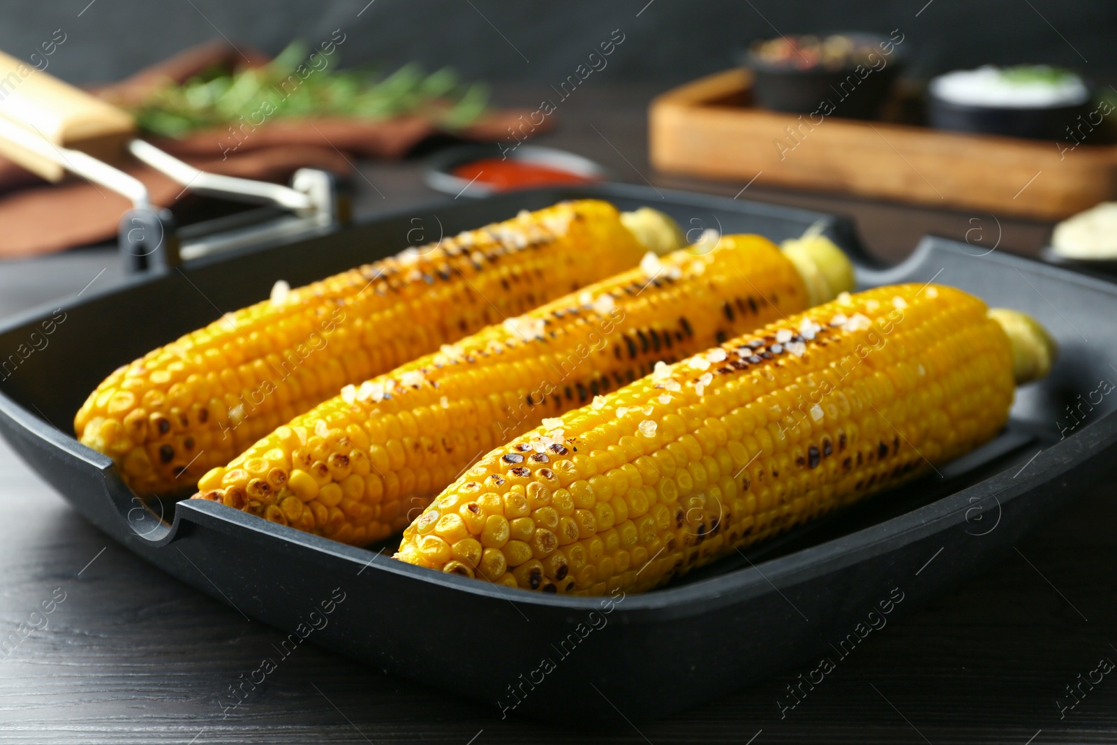 Photo of Grill pan with tasty corn on dark grey wooden table, closeup