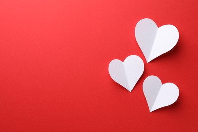 White paper hearts on red background, flat lay. Space for text