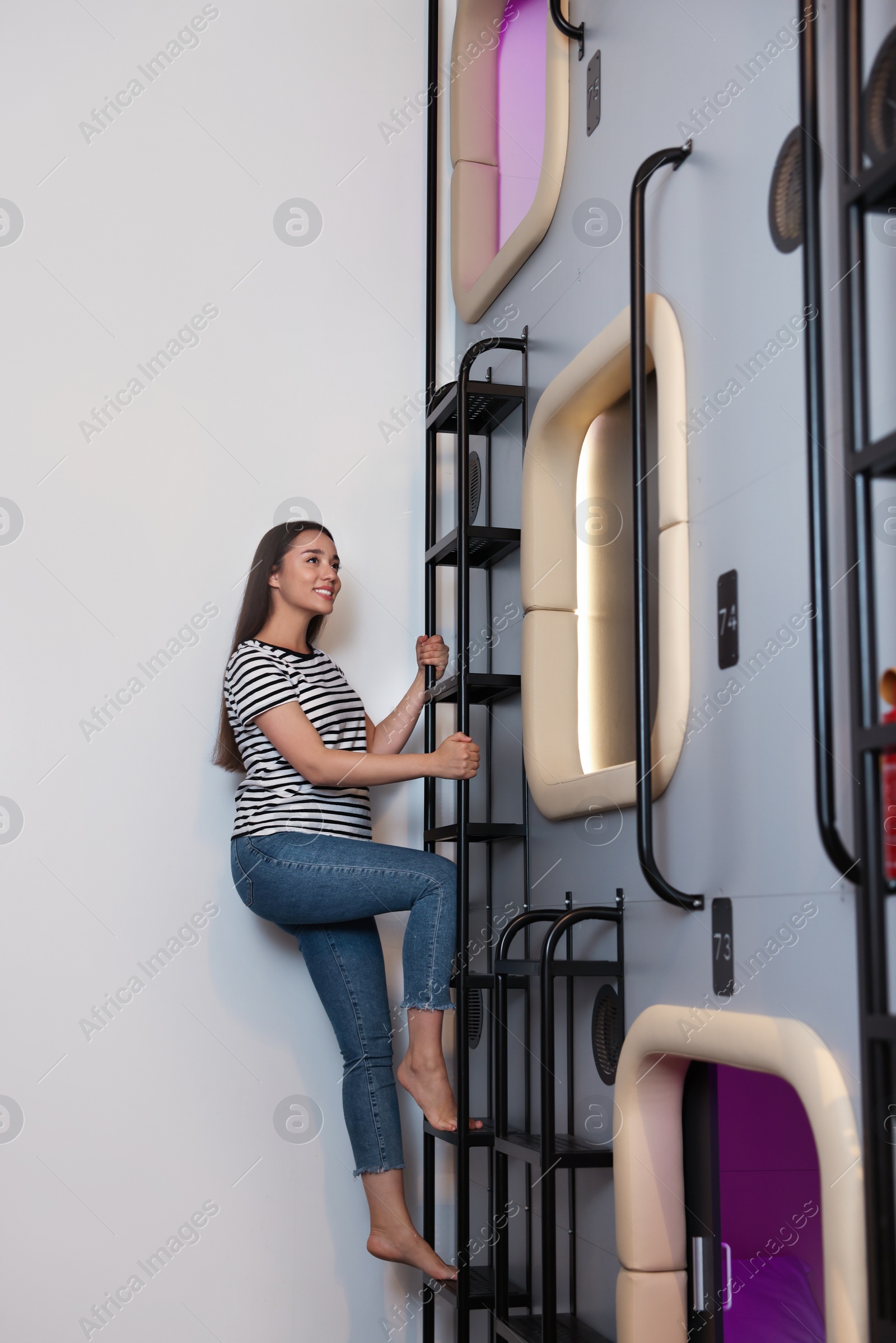 Photo of Happy young woman climbing up ladder to capsule in pod hostel