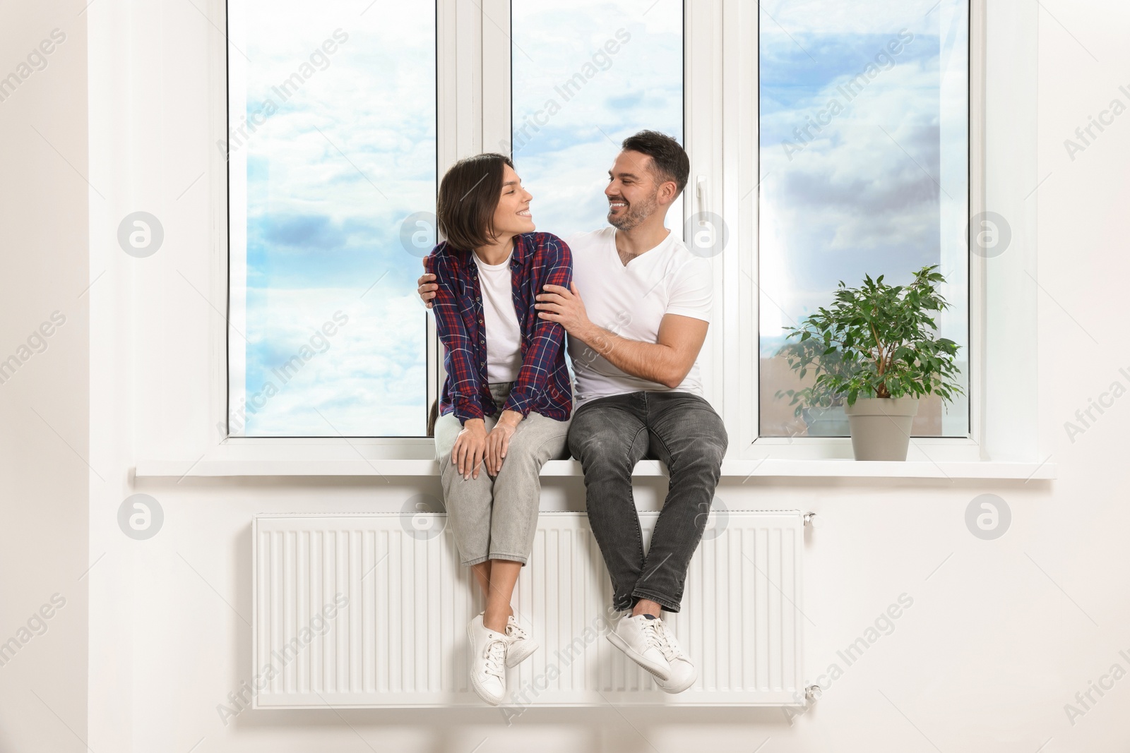 Photo of Happy couple sitting on windowsill in new apartment. Moving day