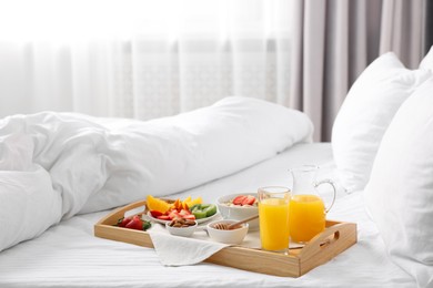 Photo of Wooden tray with tasty breakfast on bed at home