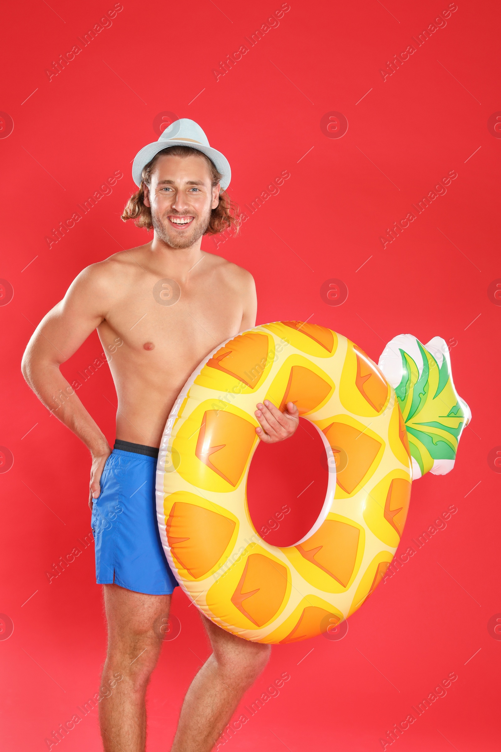 Photo of Attractive young man in beachwear with pineapple inflatable ring on red background