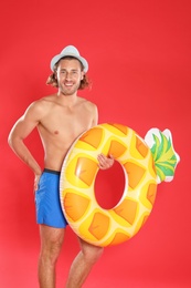 Photo of Attractive young man in beachwear with pineapple inflatable ring on red background