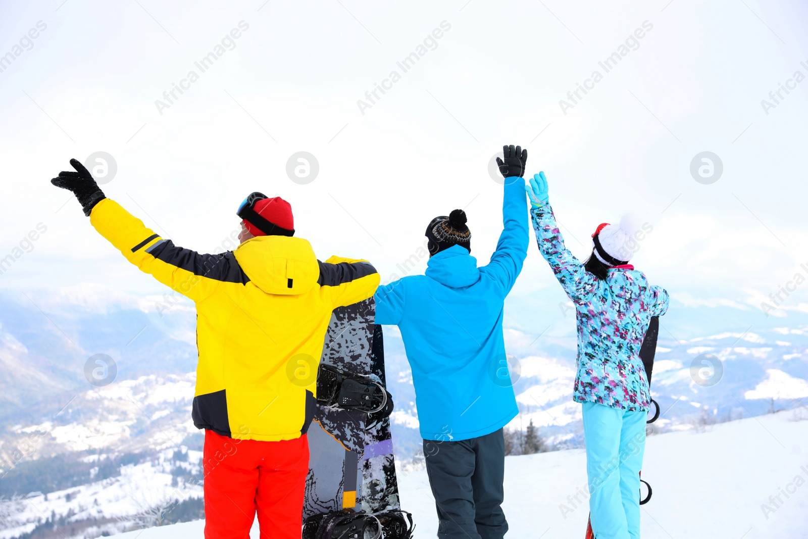 Photo of Friends with snowboards at mountain resort, back view. Winter vacation