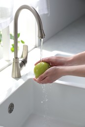 Photo of Woman washing apple over sink in kitchen, closeup
