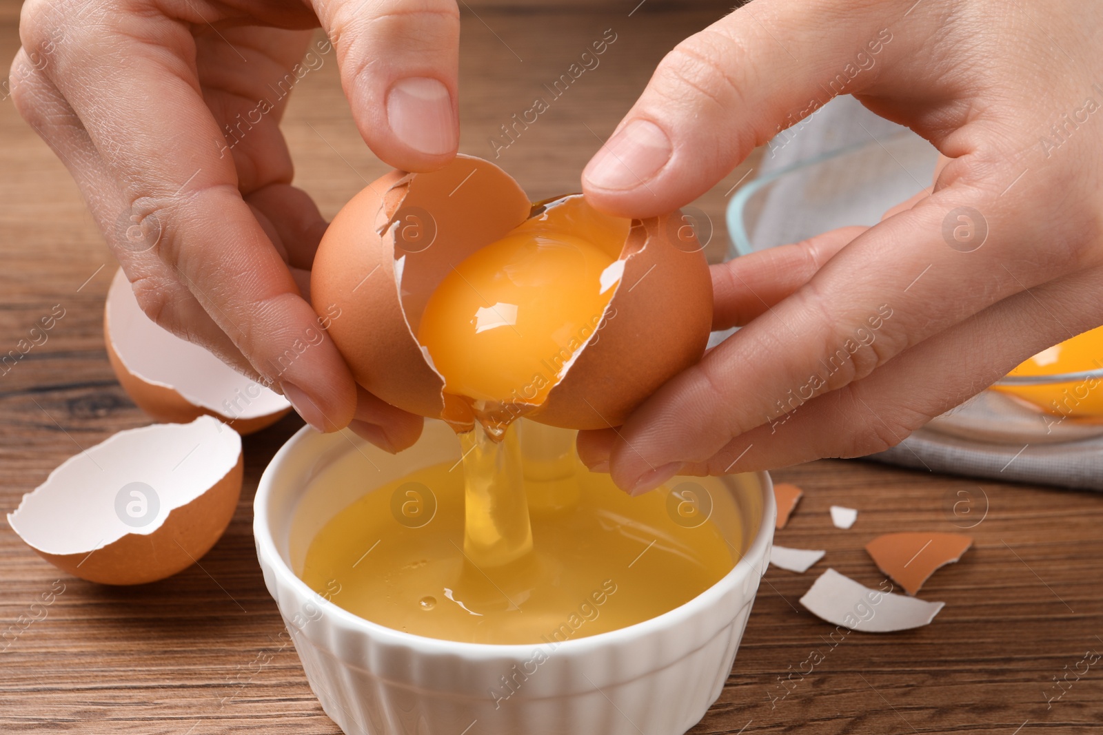 Photo of Woman separating egg yolk from white over bowl at wooden table, closeup