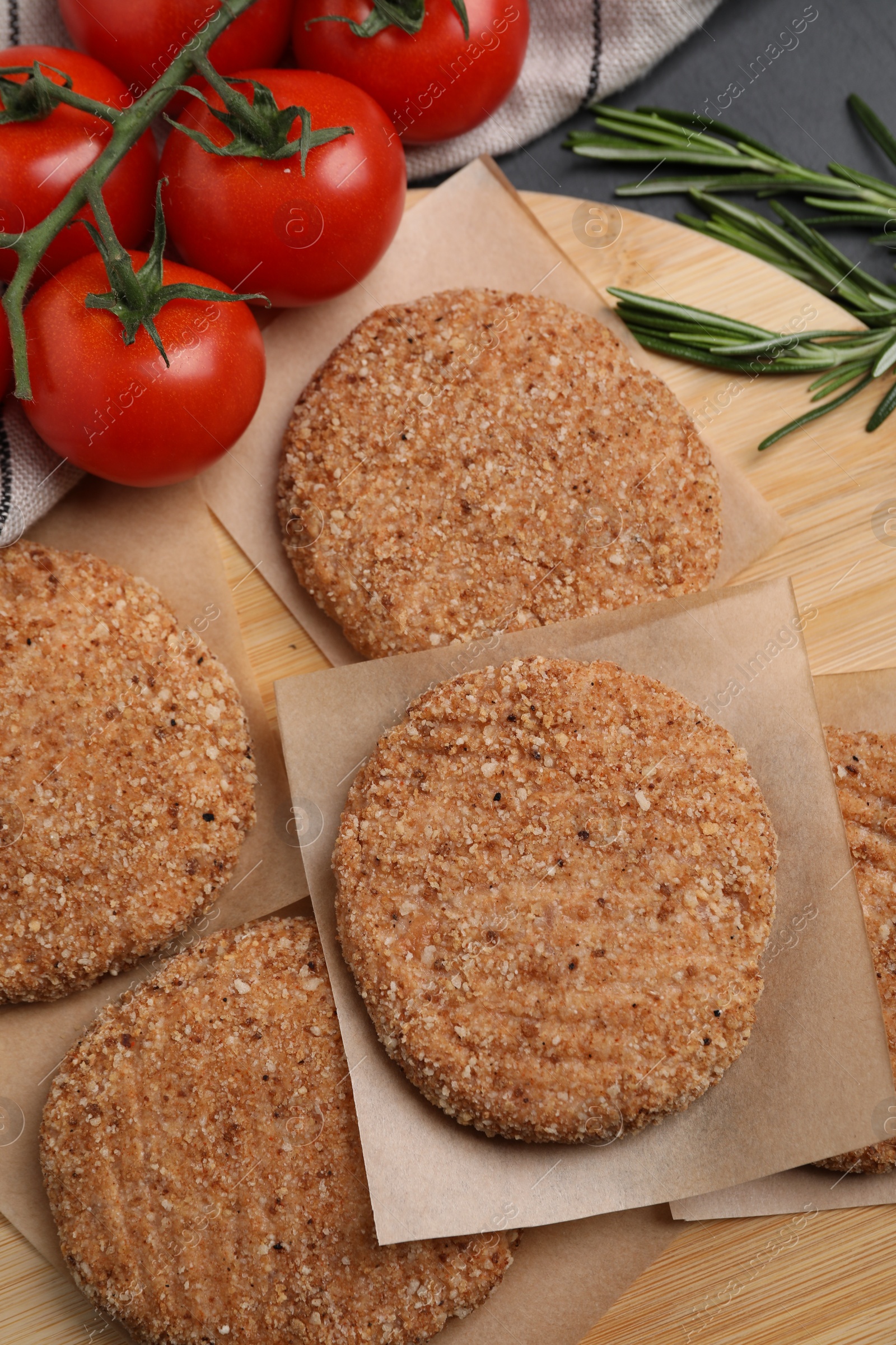 Photo of Raw vegan cutlets with breadcrumbs, tomatoes and rosemary on wooden board, above view