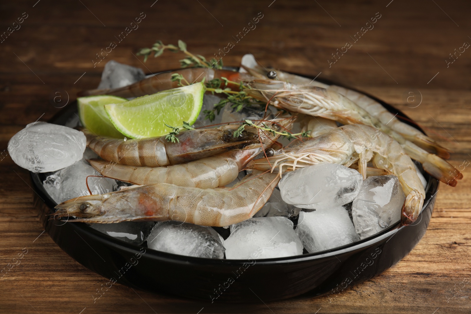 Photo of Fresh raw shrimps with lemon slices and ice on wooden table