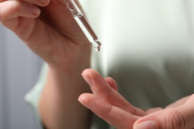 Photo of Woman applying cosmetic serum onto finger on blurred background, closeup